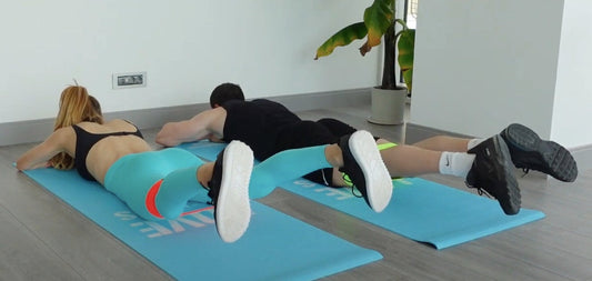 Kadın ve erkek yüzüstü pozisyonda direnç bandıyla prone abduction egzersizi yapıyor | Man and woman performing resistance band prone abduction exercise on mats.