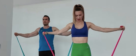 Man and woman doing resistance band lateral raises for side delts – Bir erkek ve bir kadın yan omuz kasları için direnç bandı ile lateral raise hareketi yapıyor.