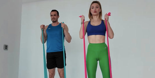 Man and woman doing resistance band hammer curls for biceps and forearms – Bir erkek ve bir kadın biseps ve ön kol kasları için direnç bandı ile hammer curl uyguluyor.